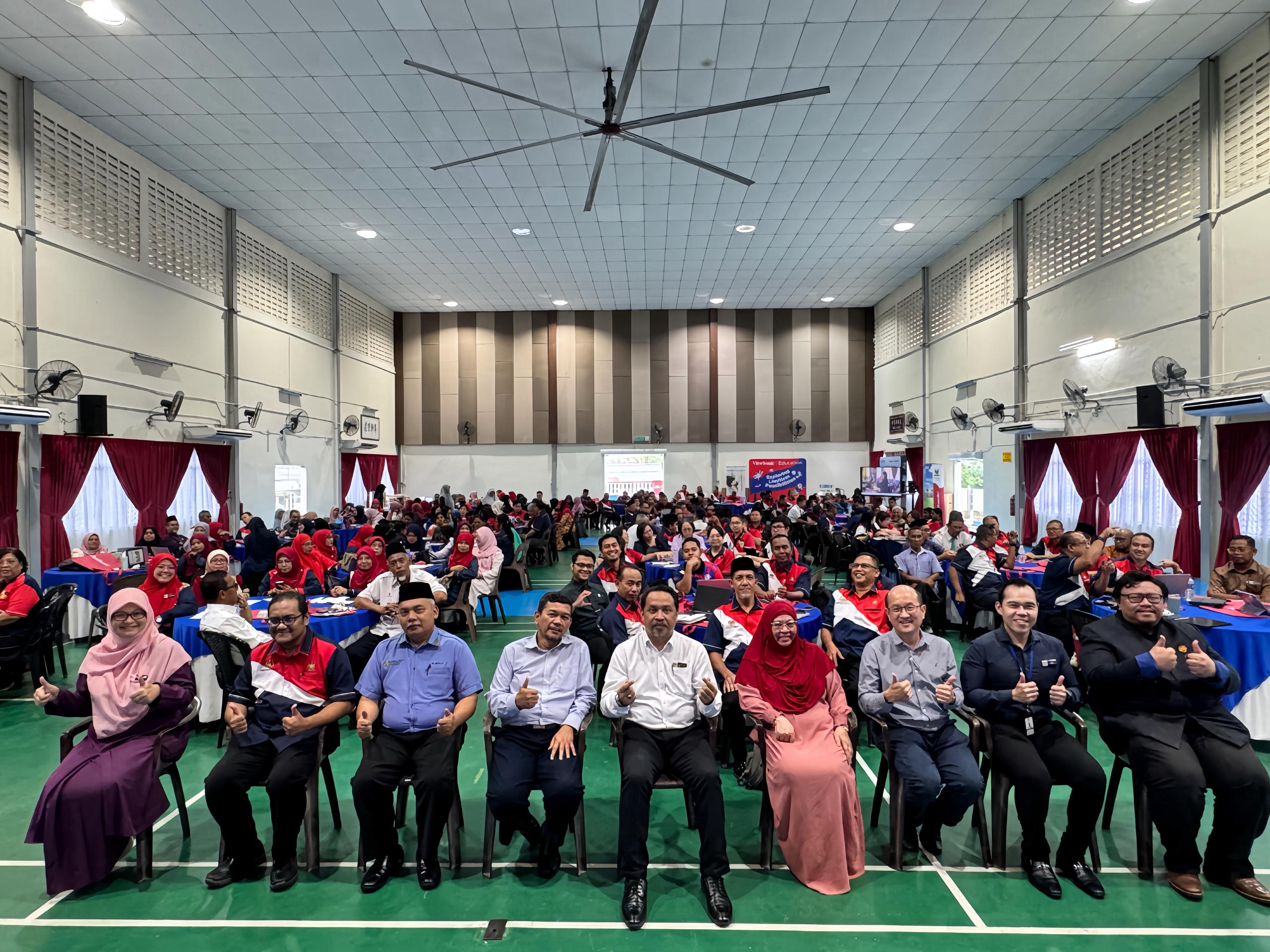 Seated with officials at a large training assembly